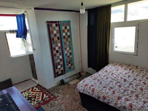Une pièce avec un lit, une fenêtre avec des rideaux, un radiateur et un mur orné d’une courtepointe.