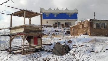 A snow-covered outdoor area with a blue building, a wooden structure, and a stone wall.