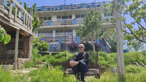 A man sitting on a swing in a garden with a building in the background. - Dede Sebo Camping (Dogubayazit)