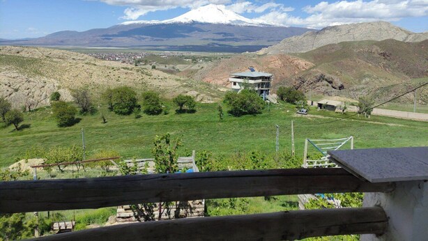 A view of a mountainous landscape with a snow-capped peak in the distance, a grassy field, and a building with a flat roof. - Dede Sebo Camping (Dogubayazit)
