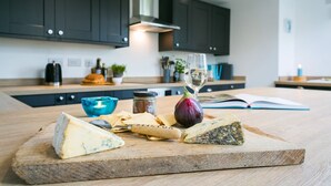 Ein Schneidebrett mit Käse, Crackern und einem Weinglas auf einer Küchenarbeitsplatte.
