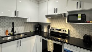 A modern kitchen with white cabinets, a black countertop, a stainless steel stove, and a microwave.