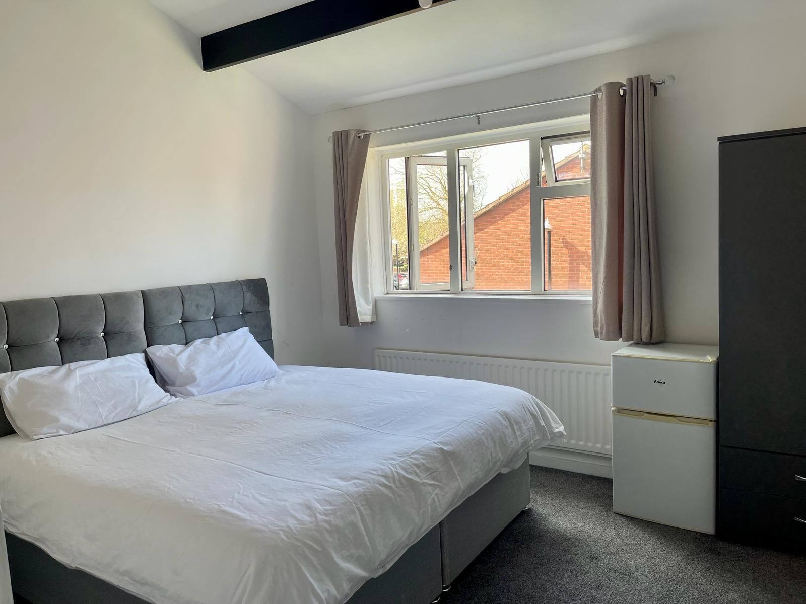 A bedroom with a bed, a radiator, a window with curtains, and a wardrobe.