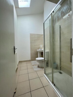 A narrow bathroom with a glass shower enclosure, a toilet, and a sink. - Homestays - Modern House Near Coventry City Centre (Coventry)