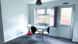 A room with a glass table and chairs, a fire exit sign, and a window with blinds. - Homestays - Modern House Near Coventry City Centre (Coventry)