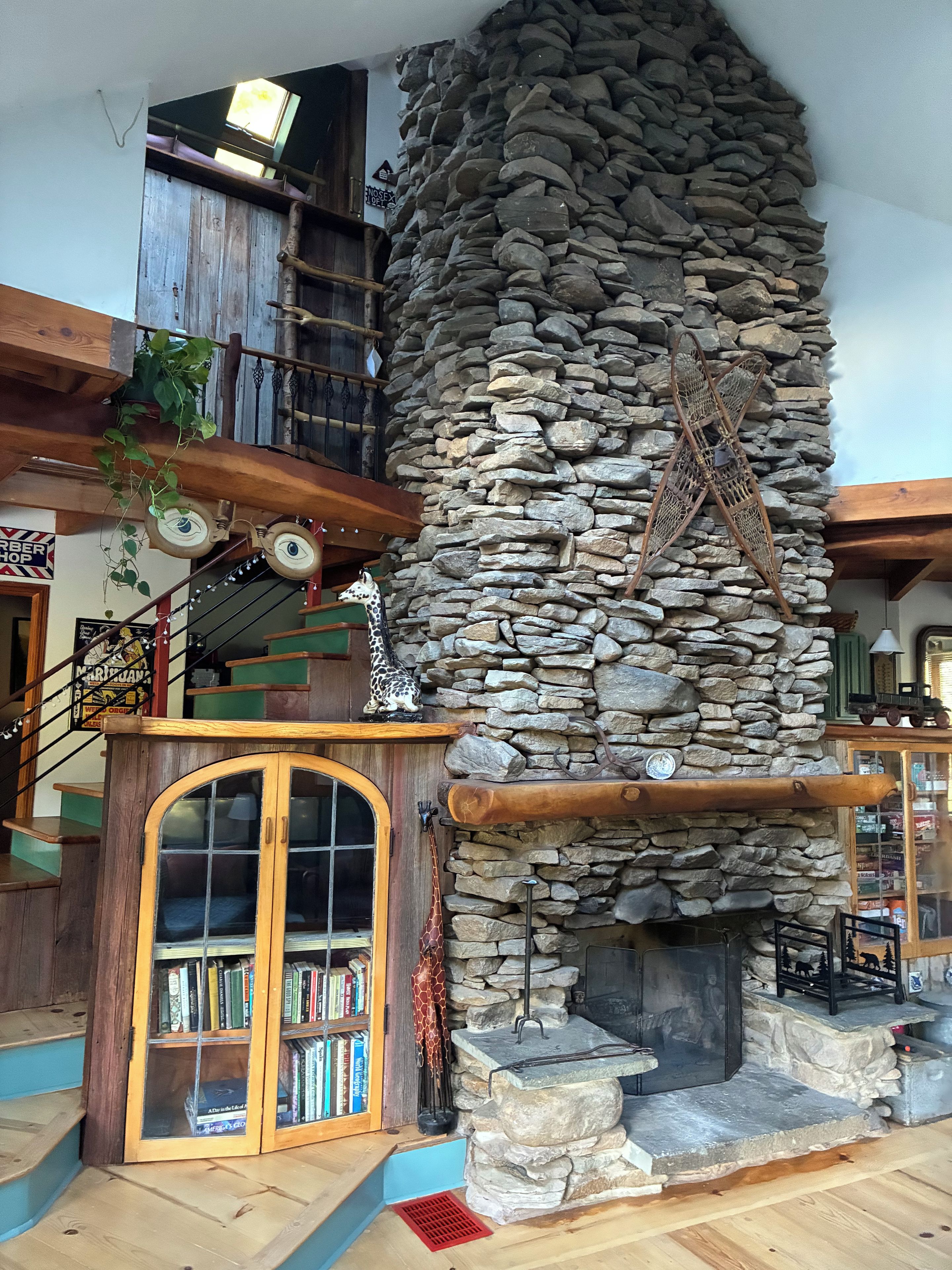 A rustic interior with a stone fireplace, wooden bookshelves, and a staircase.