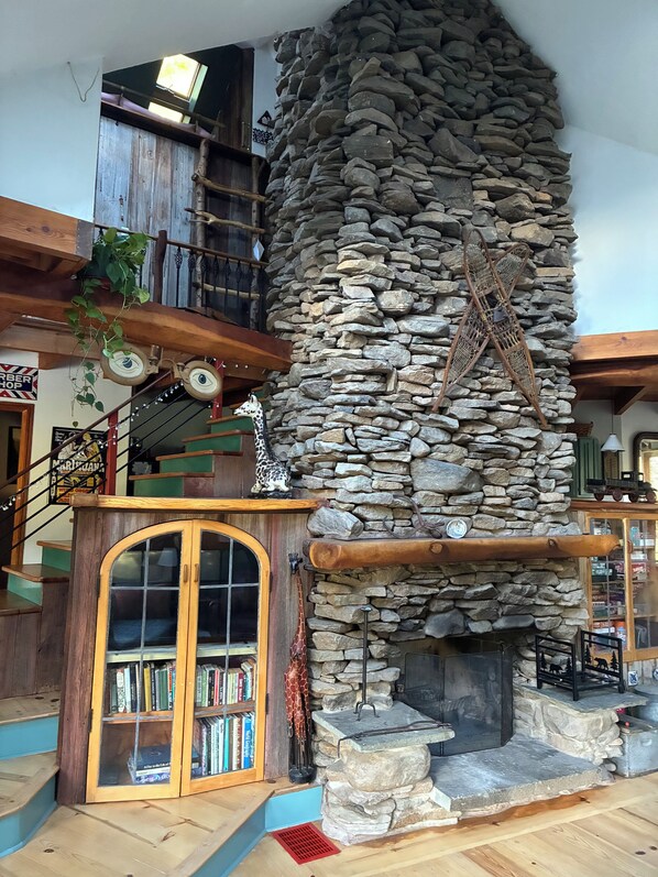 A rustic interior with a stone fireplace, wooden bookshelves, and a staircase.