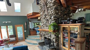 Ein gemütliches Wohnzimmer mit einem Kamin aus Stein, einem blauen Sofa und einer Holztreppe, die zu einem Erker führt.