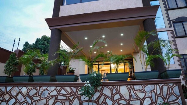 A hotel entrance with a covered outdoor area, palm trees, and a patterned wall. - ENN Business hotel (Entebbe)