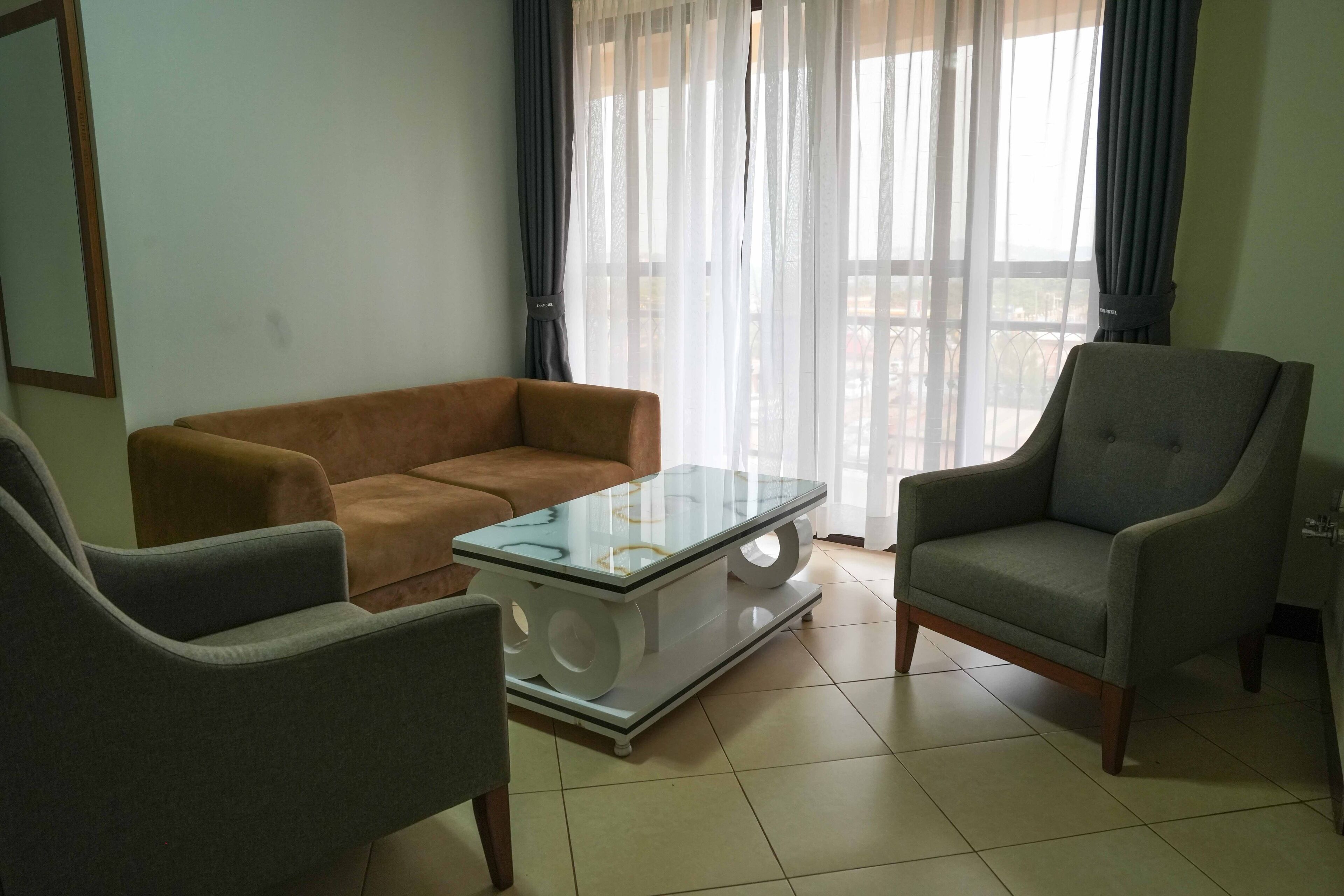 Un salon avec un canapé marron, une table basse en verre et deux fauteuils gris.