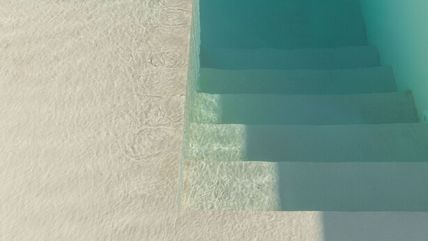 Escadaria que leva a uma piscina com água cristalina, cercada por areia branca.