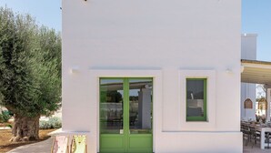 Um edifício moderno com porta e janelas verdes, um caminho pavimentado e uma árvore em primeiro plano.