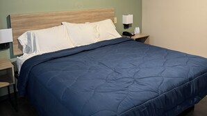 Una cama bien hecha con edredón azul, cabecera de madera y mesita de noche con lámpara.