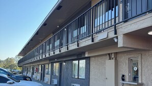 Un edificio de techo plano, con varias ventanas y un estacionamiento que incluye un coche blanco.