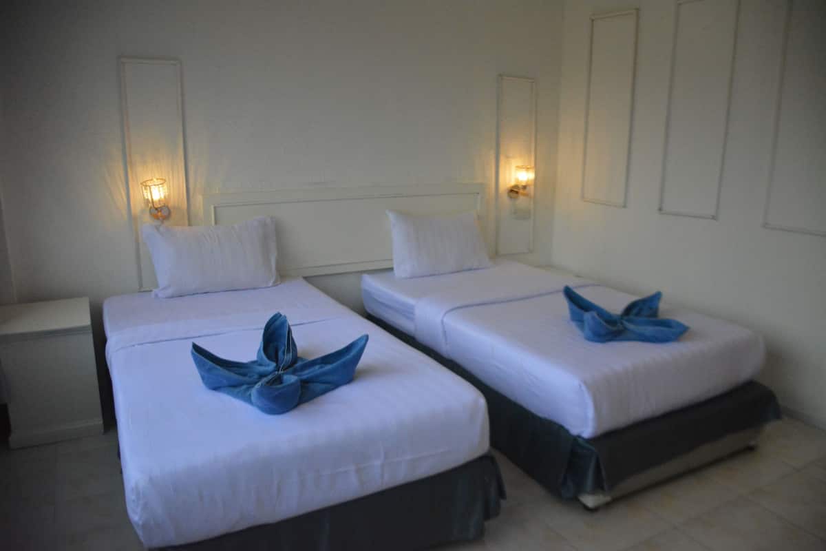 Two single beds with white linens and dark skirts, each with a blue towel on the bed.
