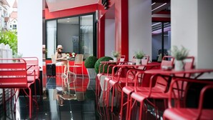 Un restaurante moderno con sillas y mesas rojas, un separador de vidrio y vista a la calle.