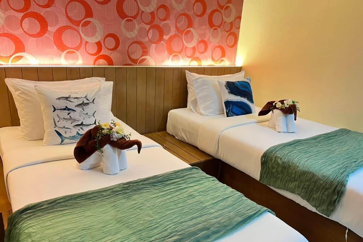 A hotel room with two beds, each with white bedding and decorative pillows. The room has a wooden headboard and a wall with a circular pattern.