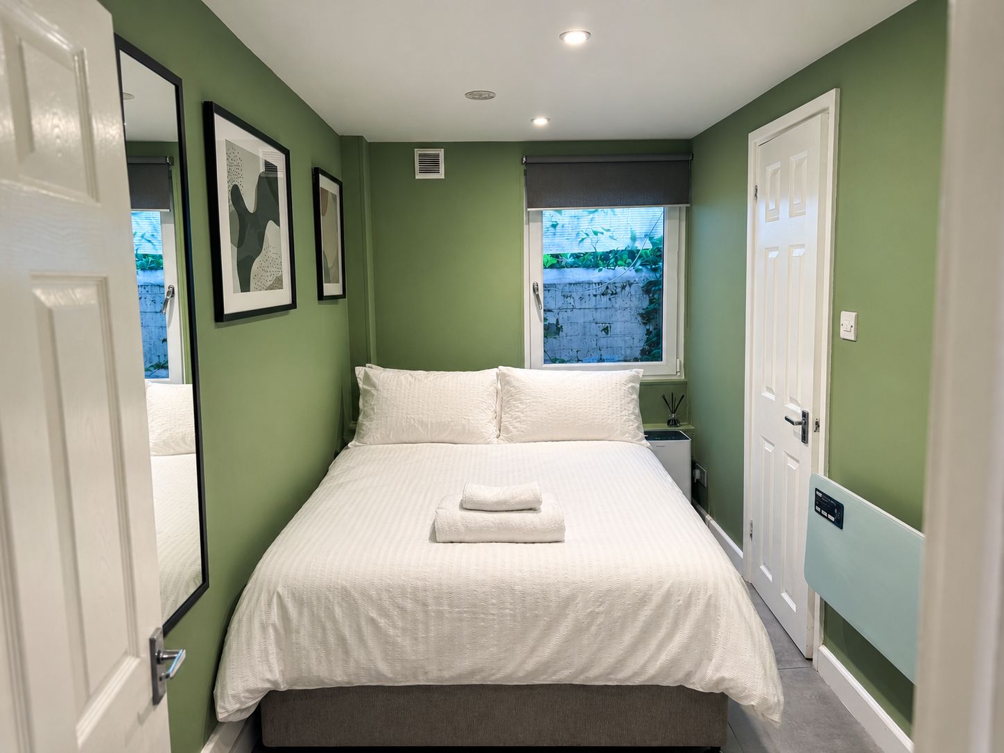 A bedroom with a bed, a window, a bedside table, and a door.