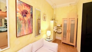 A room with a white sofa, a painting of flowers, a mirror, and a door leading to a bathroom. - Chic 2-Room Studio Retreat, Quiet Comfort in New York (New York)
