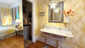 A hotel room with a bed, bedside table, lamp, and a bathroom with a marble countertop, sink, and a mirror with a chandelier. - Chic 2-Room Studio Retreat, Quiet Comfort in New York (New York)