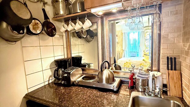 A kitchen with a dishwasher, microwave, and a sink. There are pots and pans hanging on the wall, and a window with a view of a house. - Chic 2-Room Studio Retreat, Quiet Comfort in New York (New York)