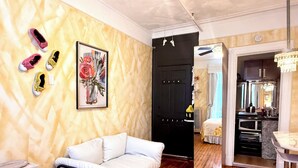 A room with a white sofa, wooden flooring, a black door, a kitchen area with a microwave, and a chandelier. - Chic 2-Room Studio Retreat, Quiet Comfort in New York (New York)