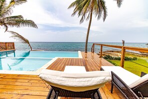 Une terrasse en bois avec une piscine, des chaises longues et une vue sur l’océan.