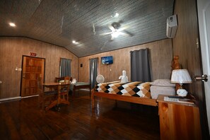Une pièce avec un plafond en bois, un lit recouvert d’une couvre-lit à motifs, un téléviseur accroché au mur et une porte en bois portant l’inscription « SORTIE ».