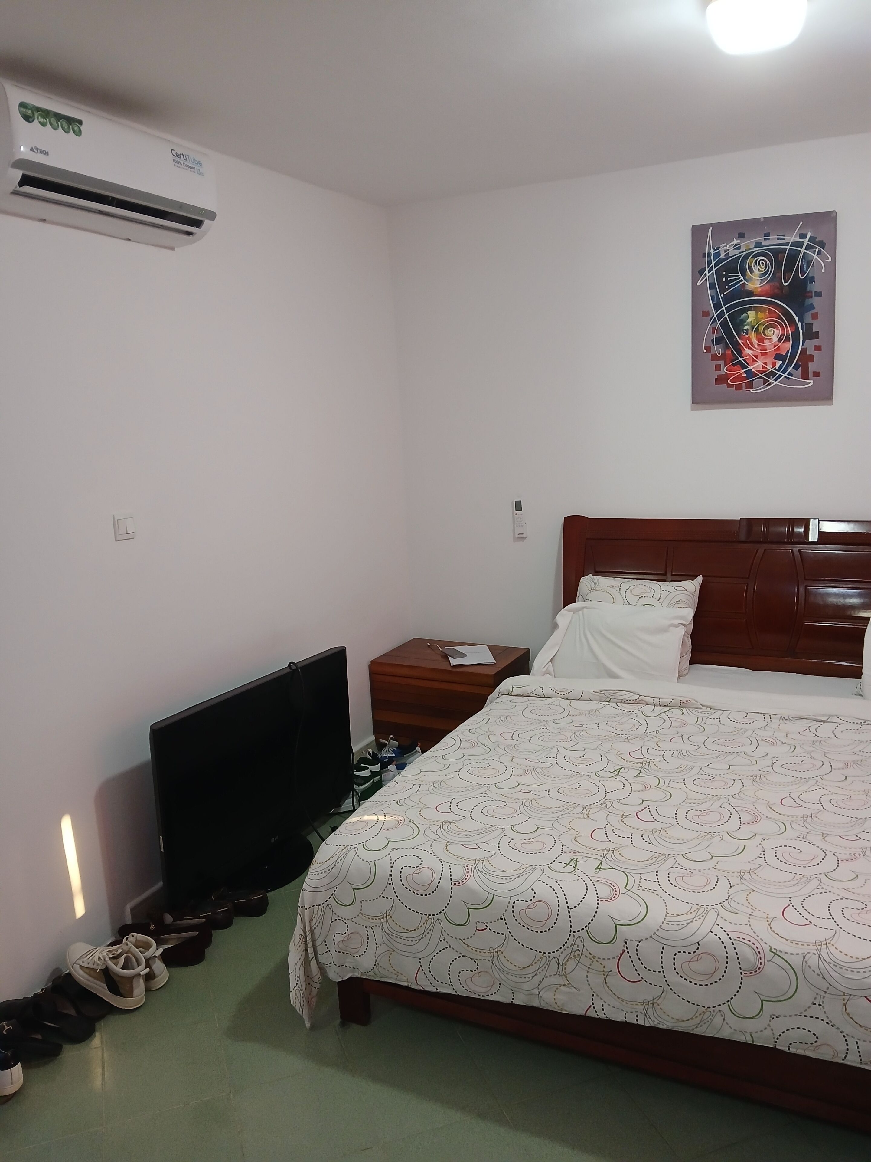 A bedroom with a bed, a television, a nightstand, and a wall-mounted air conditioner.