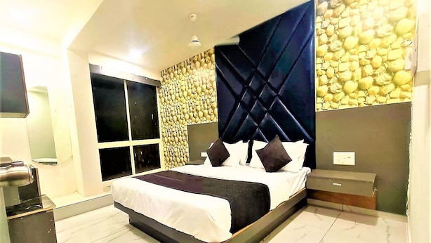 A modern bedroom with a large bed, a built-in wardrobe, and a stone wall. - Hotel Bhavya Raj (Gandhinagar)
