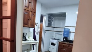A kitchen with a stove, sink, and cabinets. There are stools and a water dispenser. - Beachfront Apartment, Prime Location (Centro Cabo Frio)