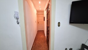 A narrow hallway with a carpeted floor, a white door at the end, and a wall-mounted TV. - Beachfront Apartment, Prime Location (Centro Cabo Frio)