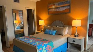 A hotel room with a bed, two bedside lamps, a nightstand, a mirror, and a painting on the wall.