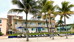 A beachfront hotel with multiple balconies, palm trees, and lounge chairs on the sand.