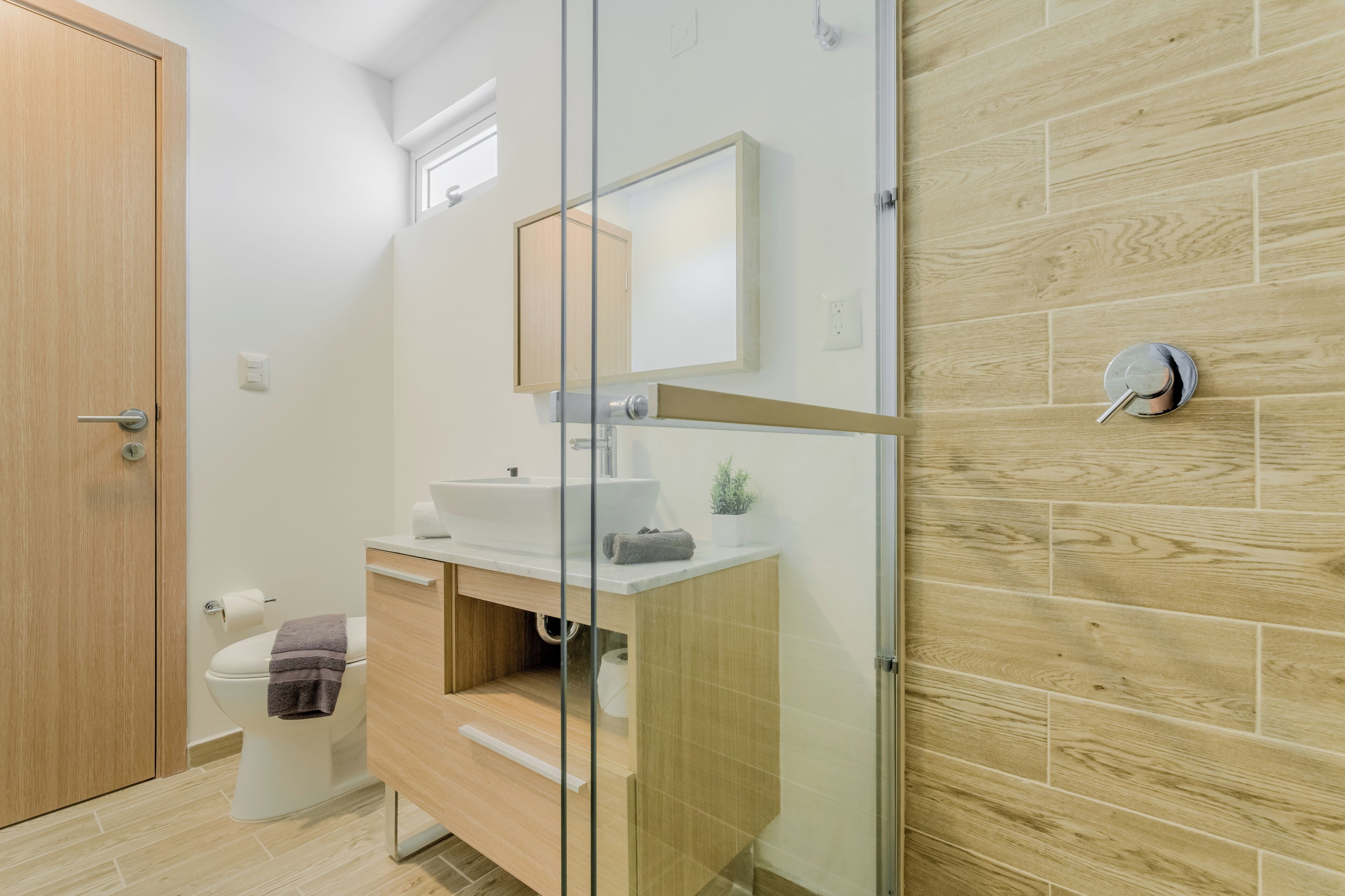 A modern bathroom with a wooden vanity, a glass shower enclosure, and a white toilet.