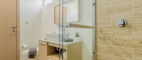 A modern bathroom with a wooden vanity, a glass shower enclosure, and a white toilet.
