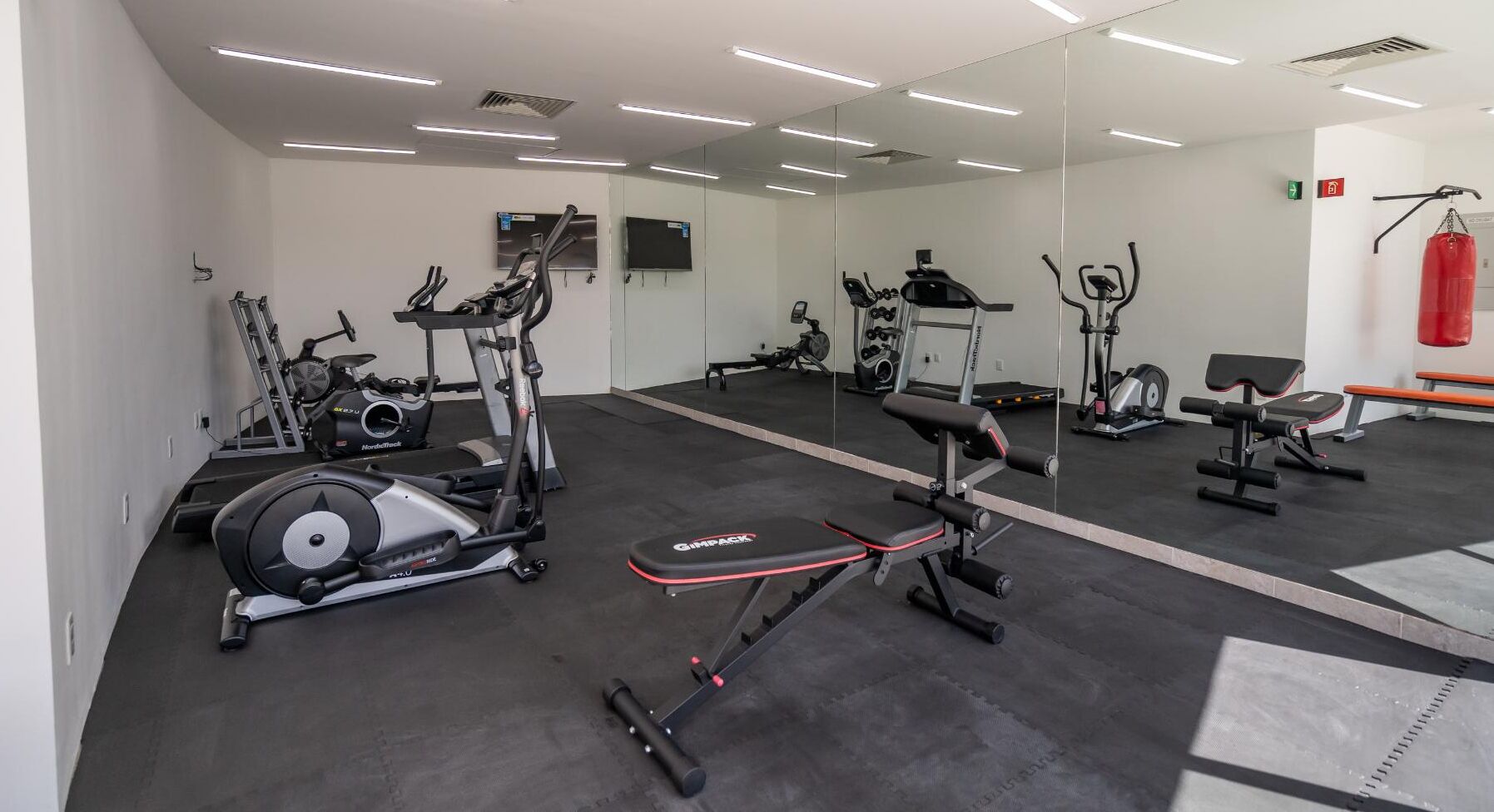 Un gimnasio con máquinas de cardio, equipo de levantamiento de pesas y una banca.