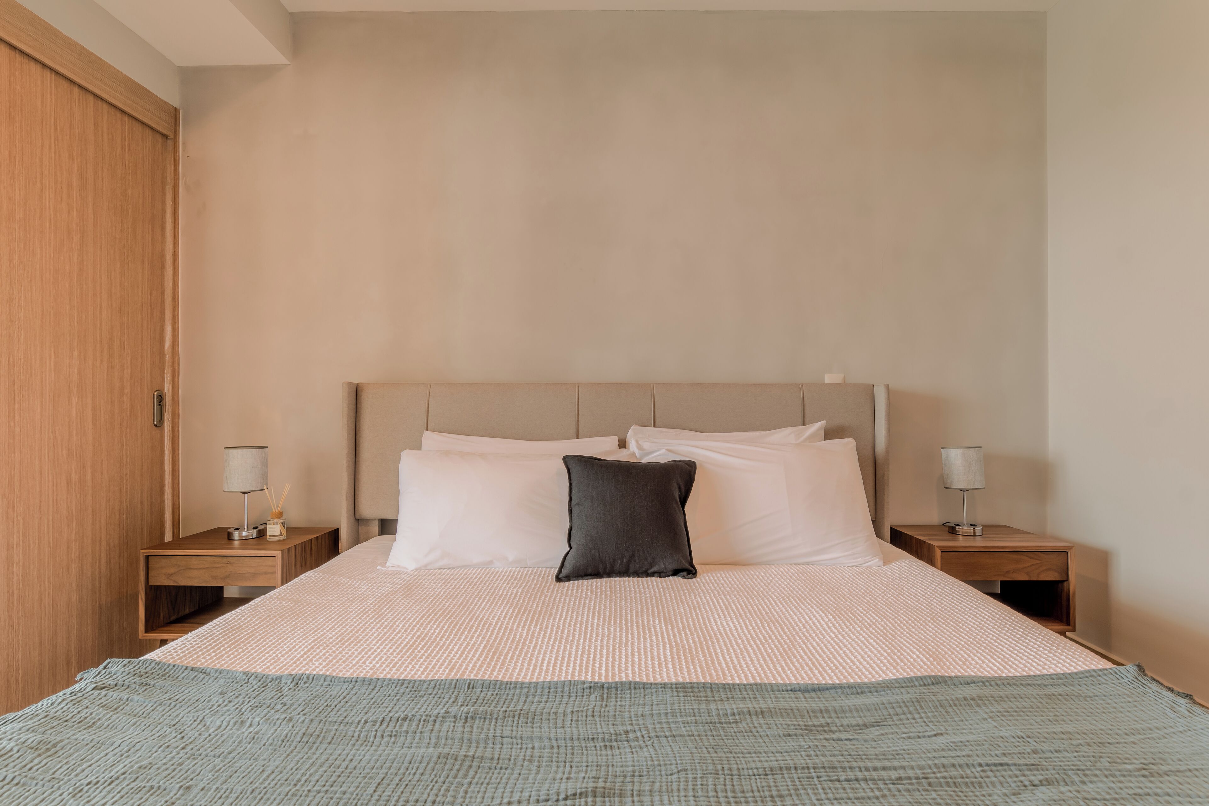 A neatly made bed with a beige headboard, two bedside tables with lamps, and a wooden wardrobe.