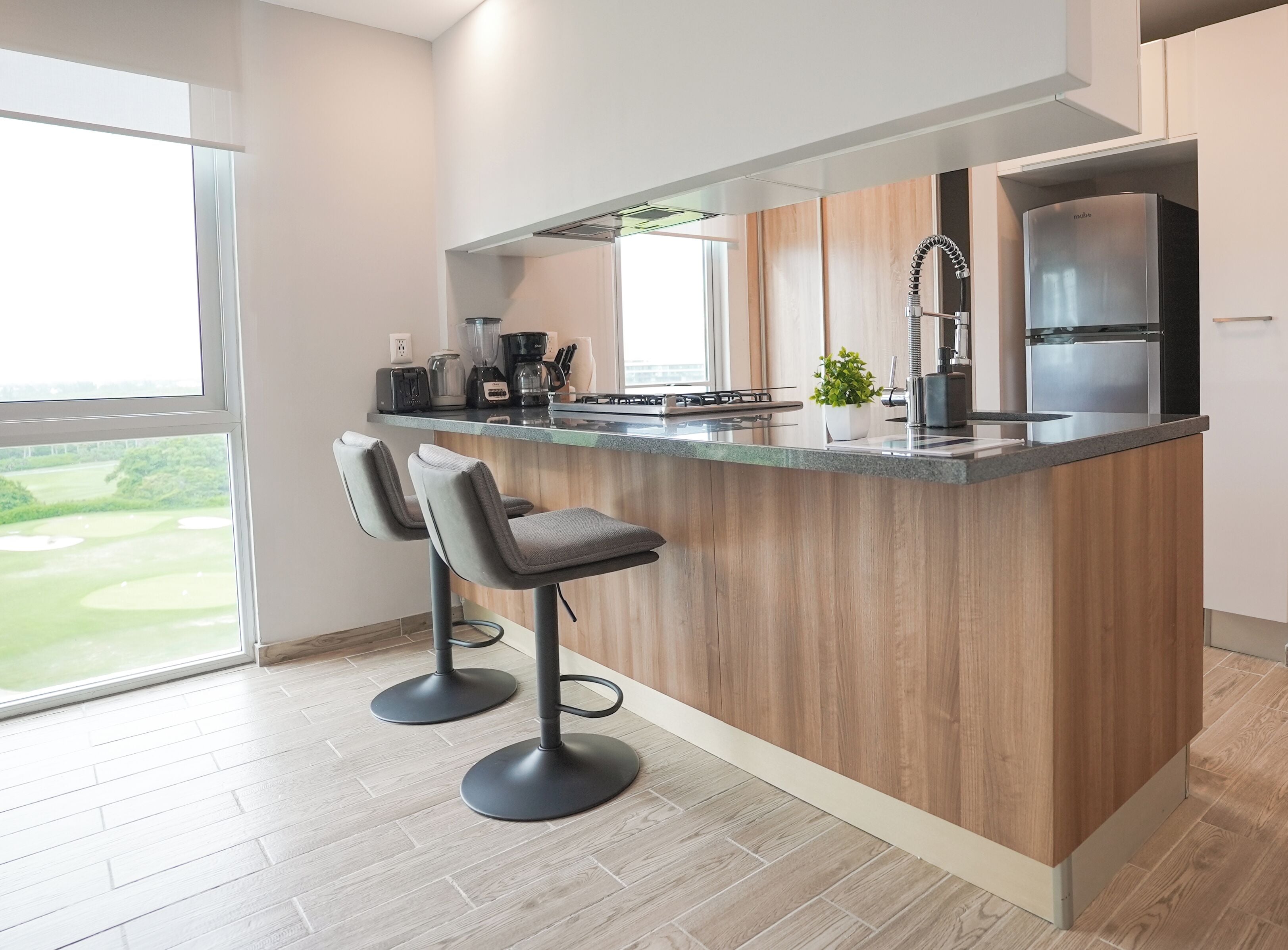 A modern kitchen with a wooden island, bar stools, a stainless steel refrigerator, and a view of a golf course.