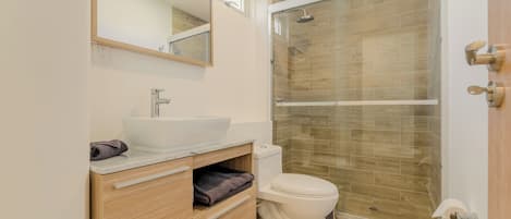 A modern bathroom with a glass-enclosed shower, a white sink, and a wooden vanity.