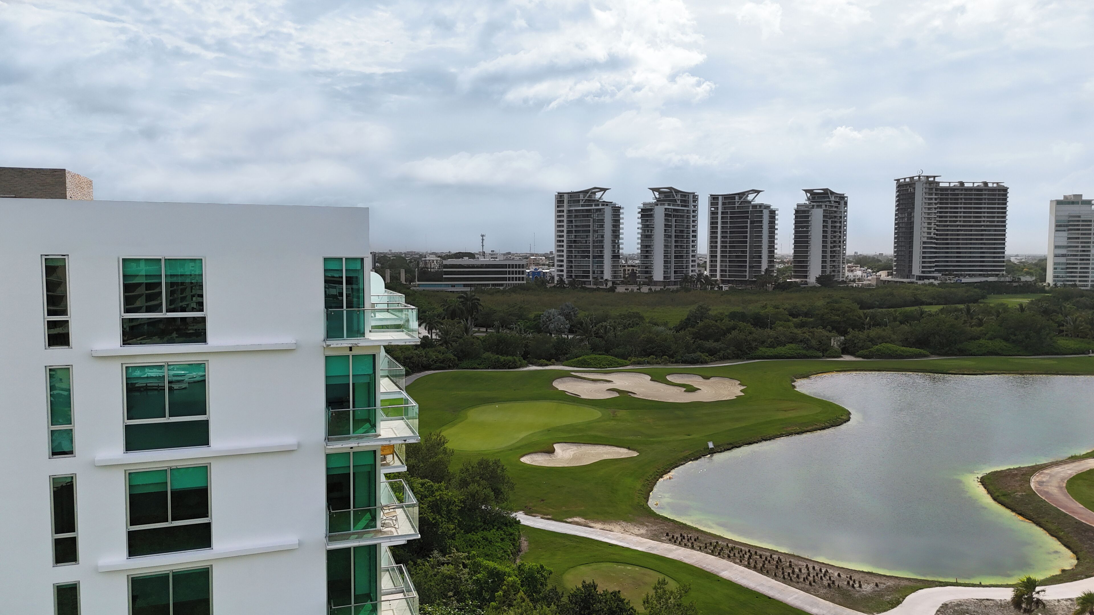 Um edifício moderno com várias varandas e vista para um campo de golfe com bunkers de areia e um lago.