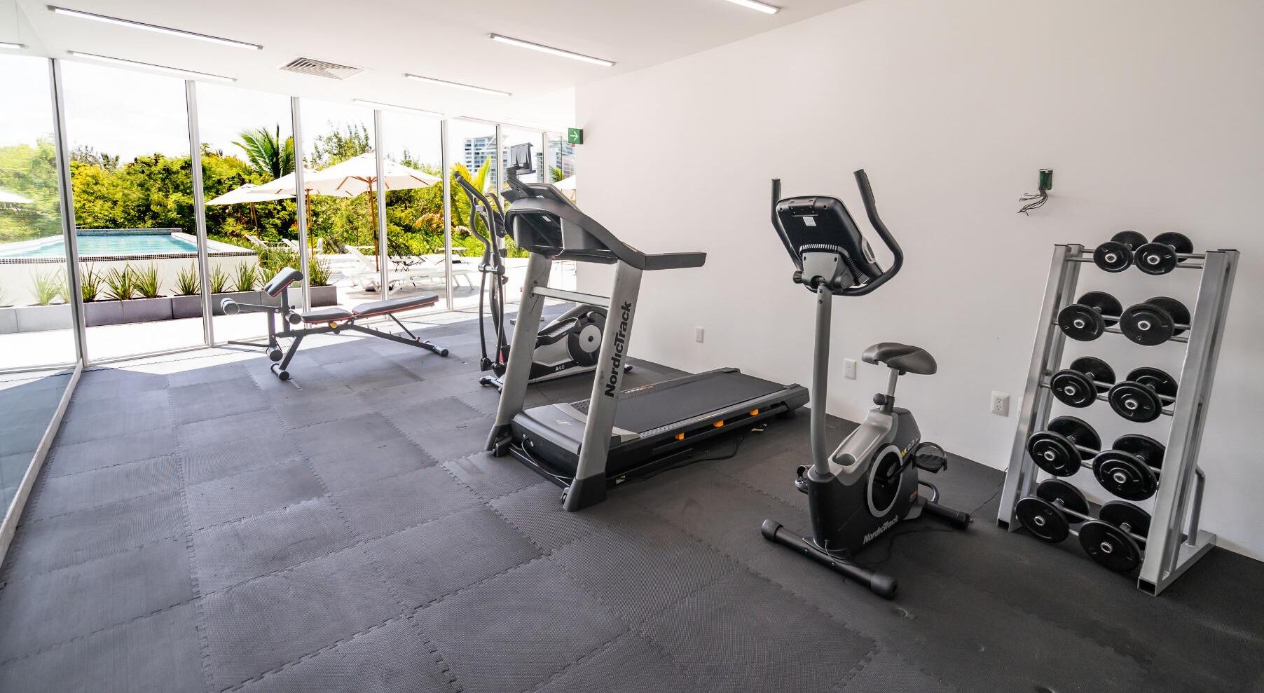 A gym with treadmills, an elliptical, and a rack of dumbbells.