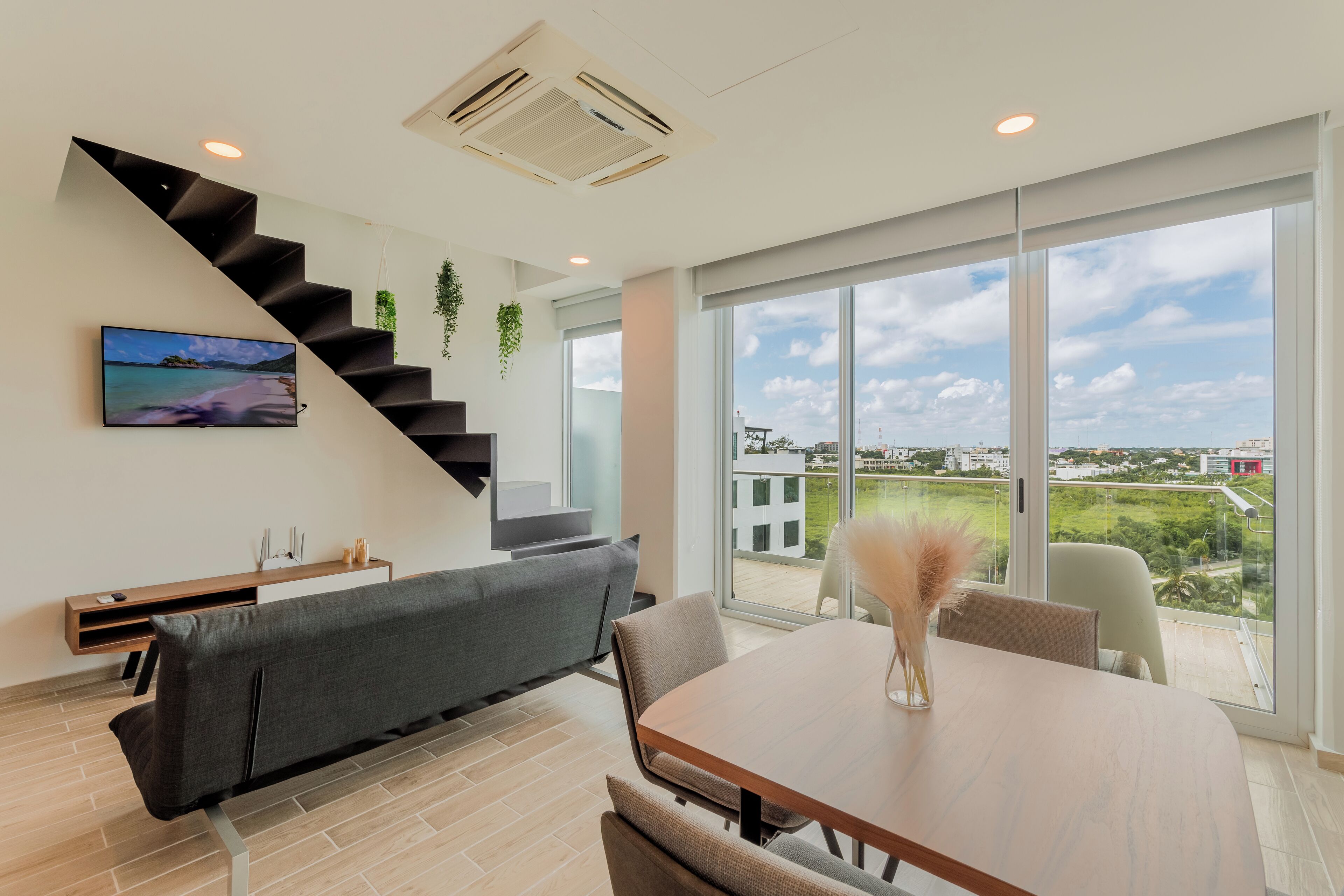 Un salon moderne avec un escalier, un coin repas et une grande fenêtre donnant sur la ville.