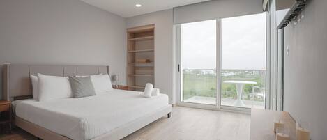 A modern bedroom with a large bed, built-in shelving, a balcony with a table, and a view of the outdoors.