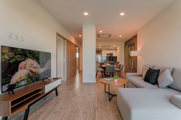 A modern living room with a flat-screen TV, a grey sofa, a coffee table, and a dining area with chairs and a table. - EHDEN Vacation Suites Puerto Cancún (Cancun)