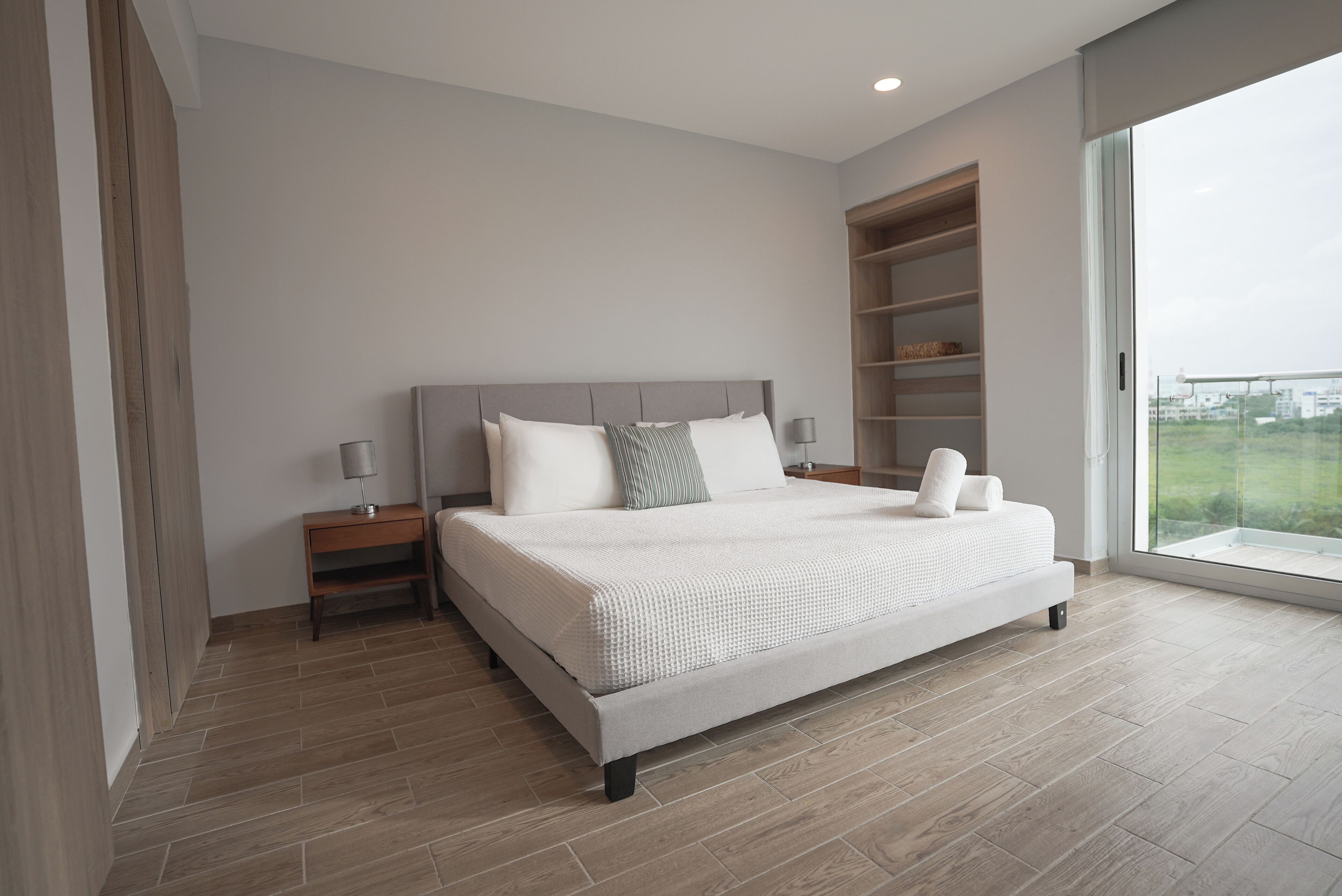 Quarto moderno com uma cama grande, piso de madeira e estante embutida.