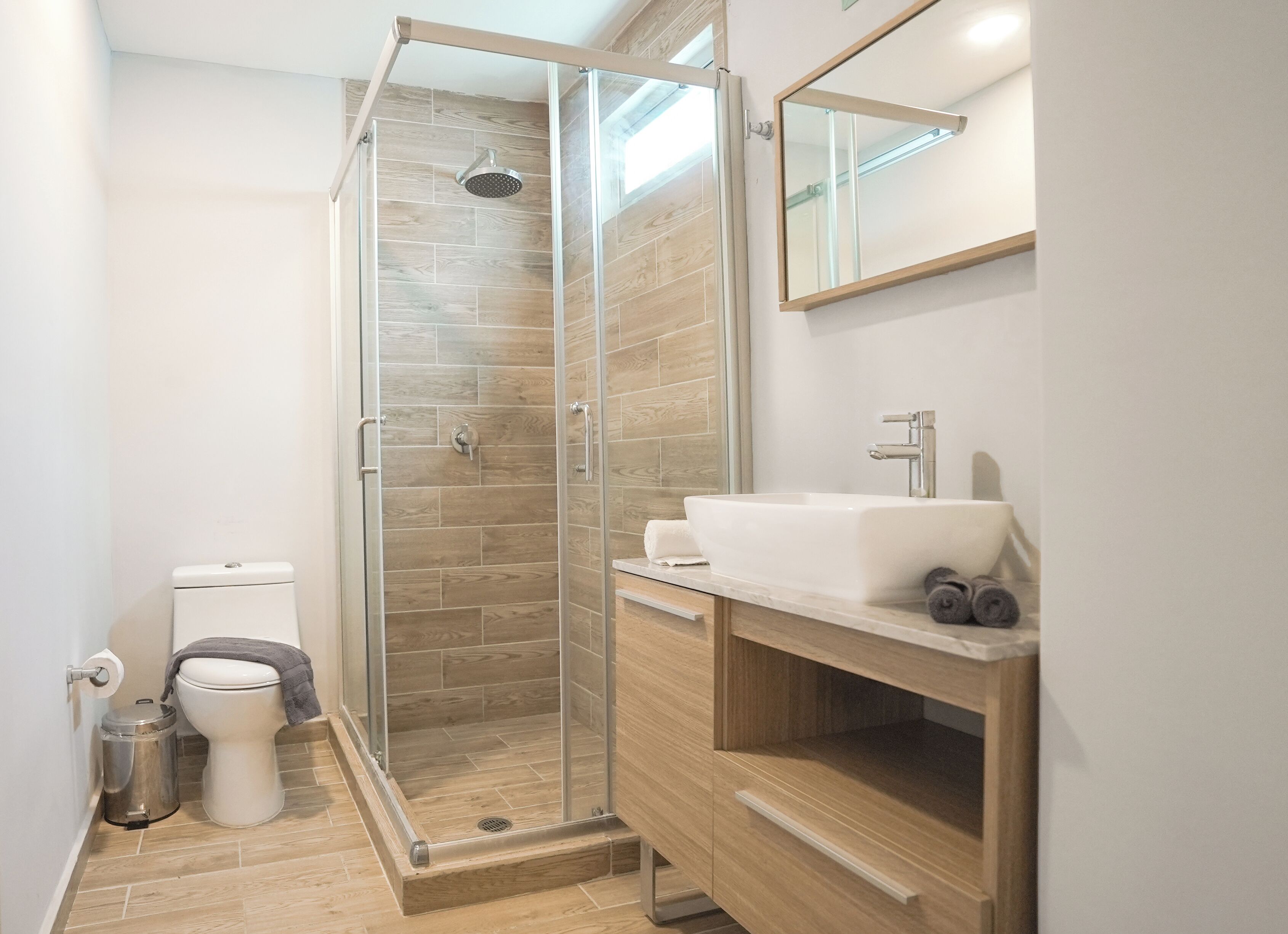 A modern bathroom with a glass-enclosed shower, a toilet, and a vanity with a sink and mirror.