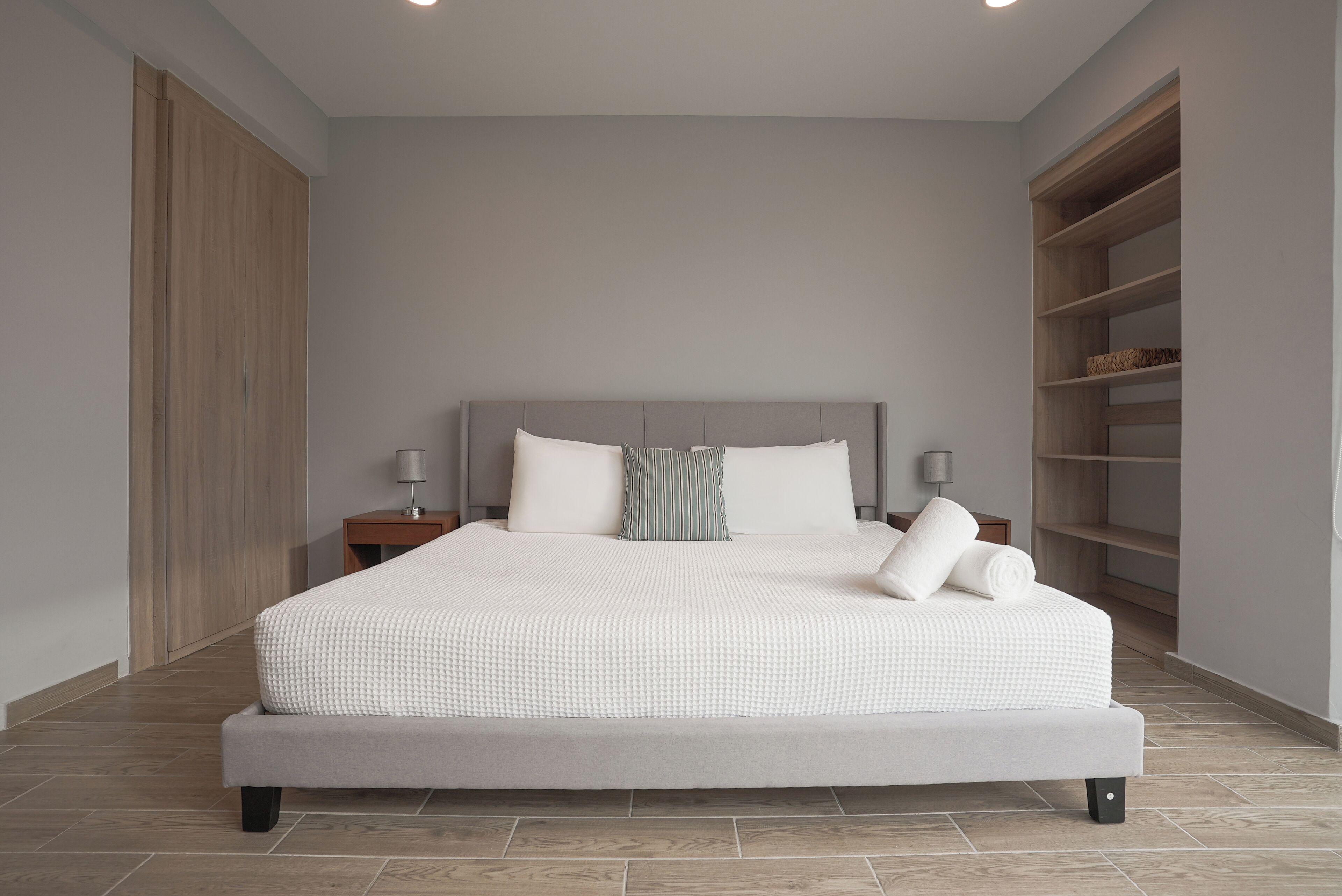A modern bedroom with a large bed, a nightstand, a lamp, and built-in shelving.