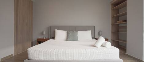 A modern bedroom with a large bed, a nightstand, a lamp, and built-in shelving.