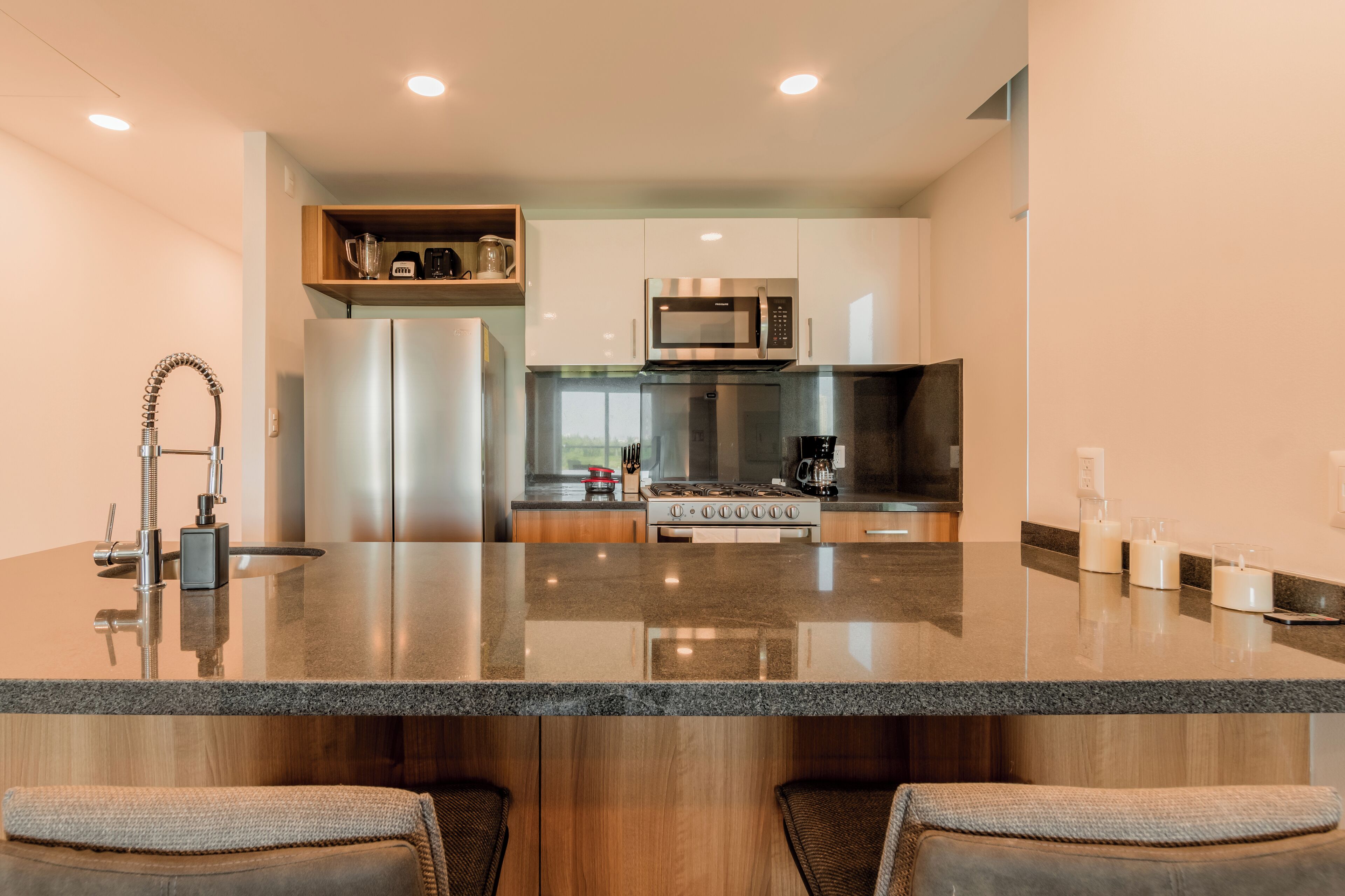 A modern kitchen with a central island, stainless steel appliances, and a wooden upper shelf.